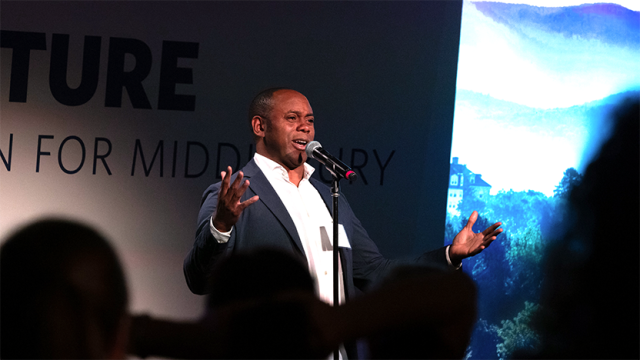 Kazem Abdullah in white shirt and dark grey jacket, telling his story with arms in an open gesture