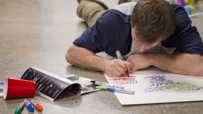Student lying on the floor working with markers