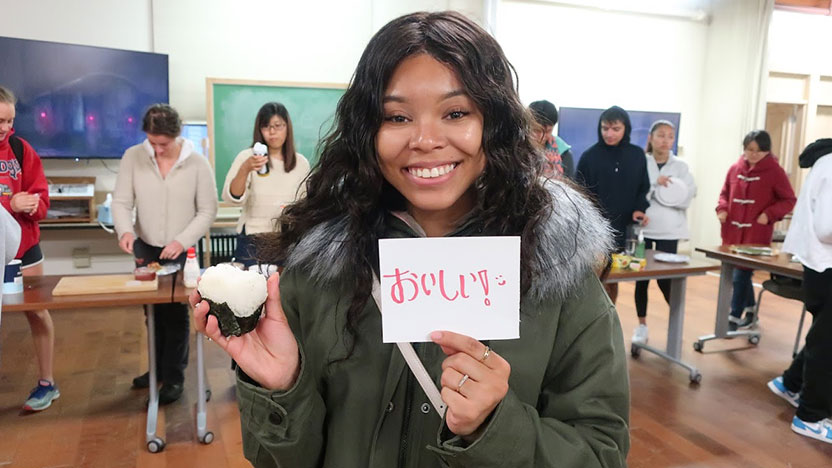 A Japanese students holds a sign, smiling for the camera