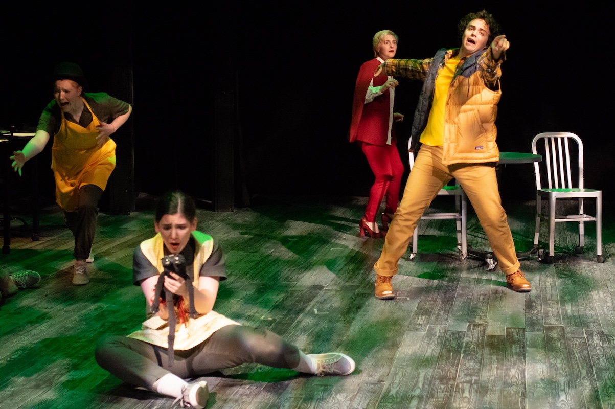 An actor points at the distance as another one falls and a third actor crouches on the ground holding a sock puppet