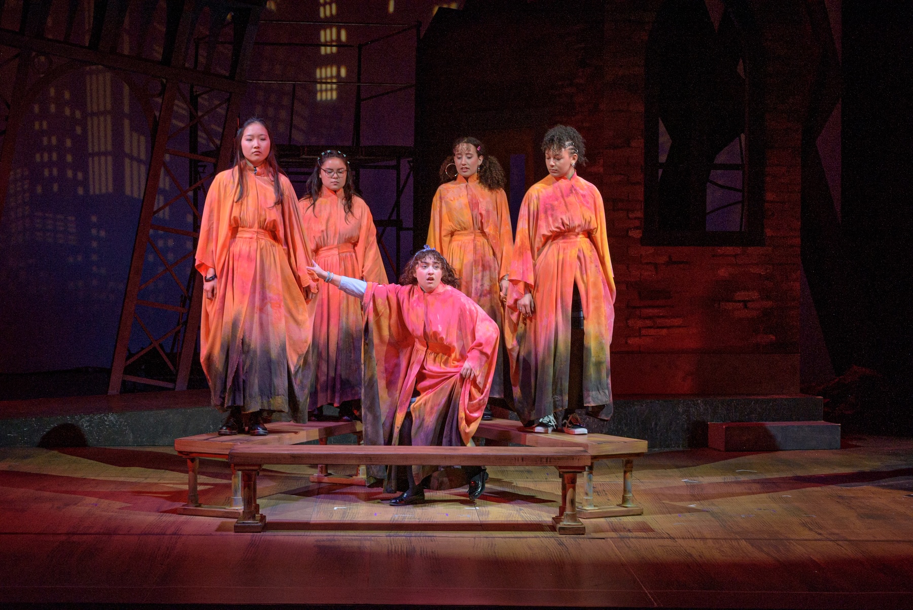 Five actors covered in fabric designed like fire, looking out at the audience as one of them speaks