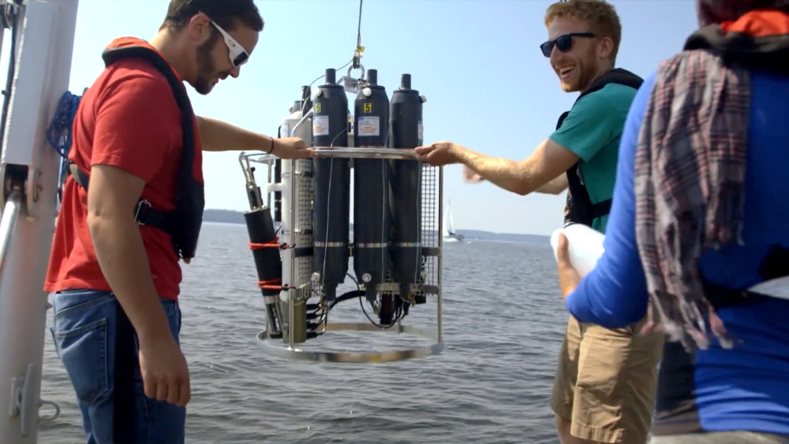 Students putting oxygen tanks into water off the side of a boat.