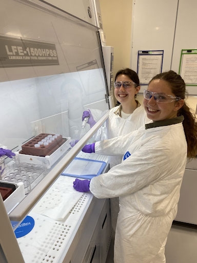 Two students in lab coats and safety gear in the FOR@M lab