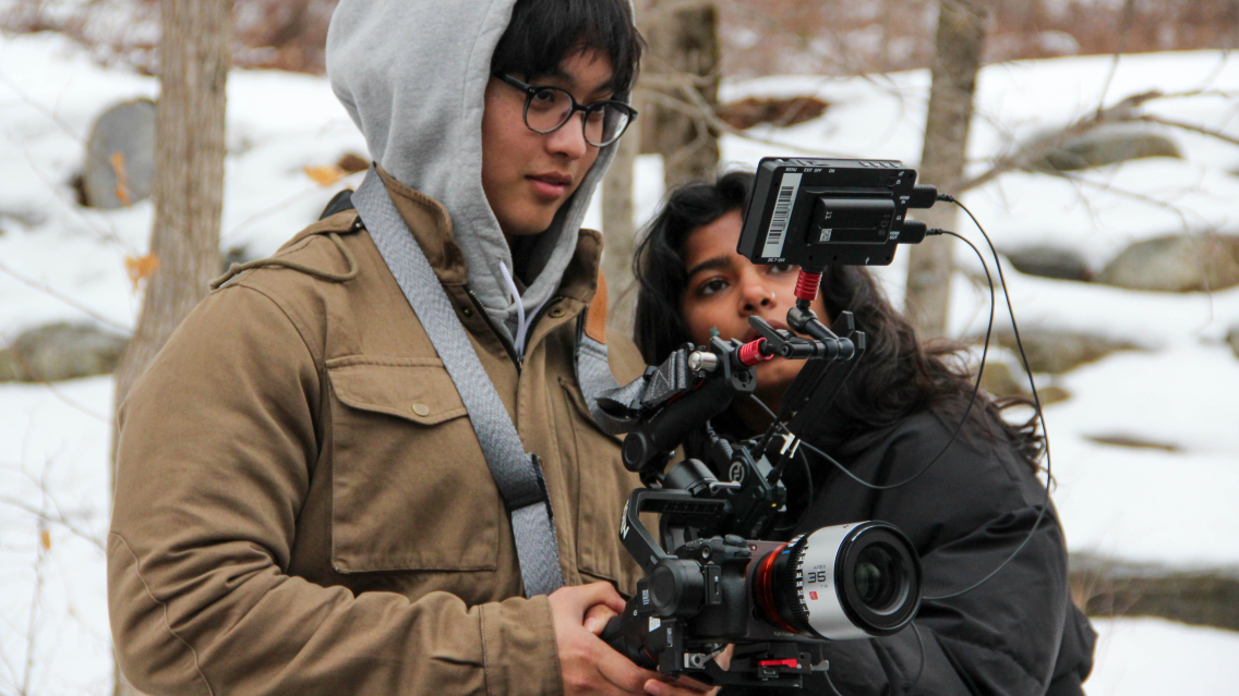 Two students operate a video camera in the snow