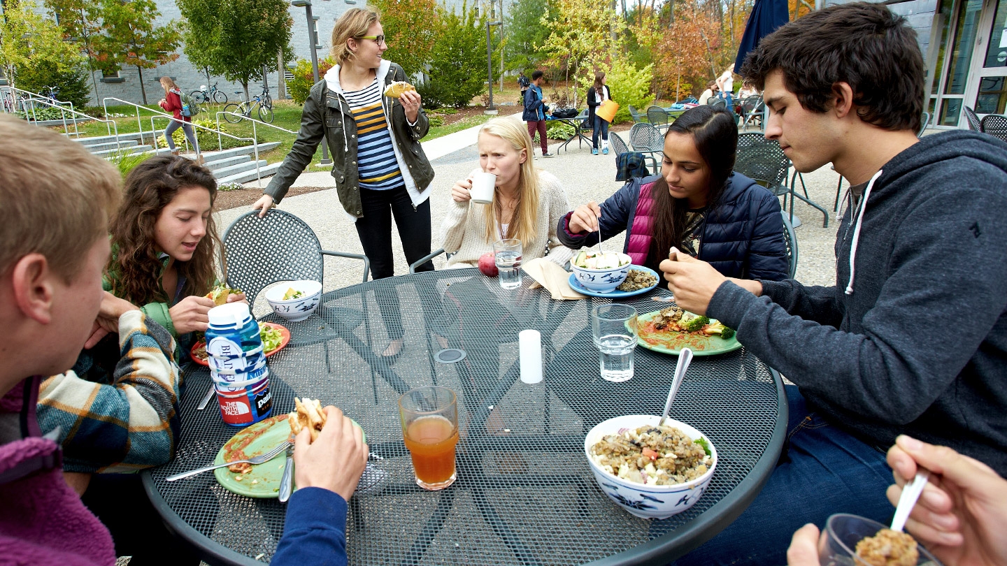 Several Middlebury students sit at an outdoor patio table talking and eating a meal.