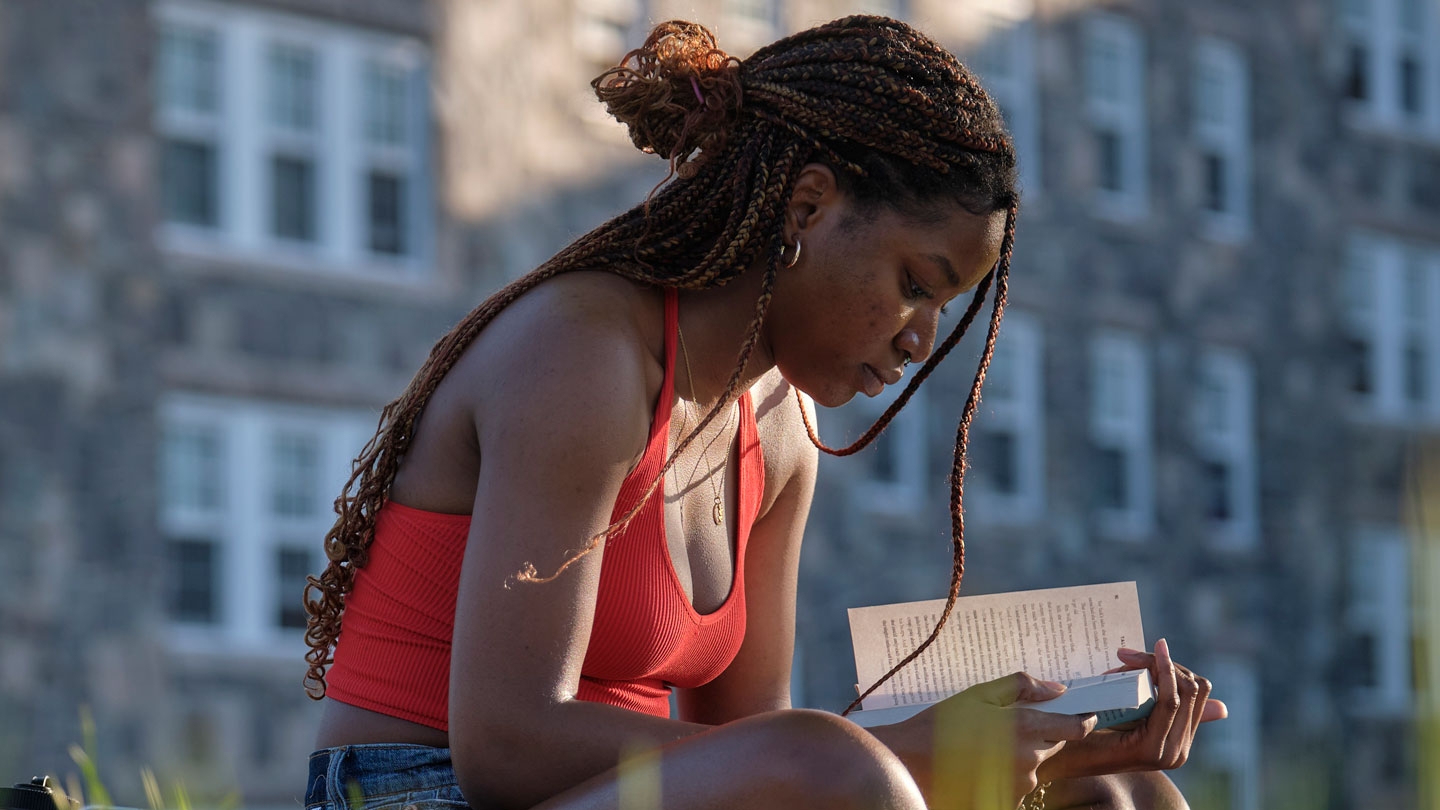 Girl reading in the grass outside a dorm.