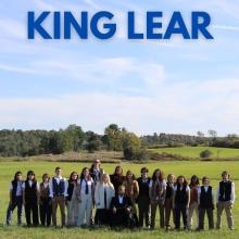 Cast of King Lear stand in a field in tableau, staring at the camera stoically.