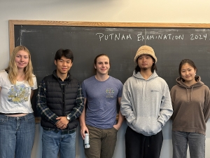 five students standing in front of a blackboard with the words Putnam Examination 2024 written on the board