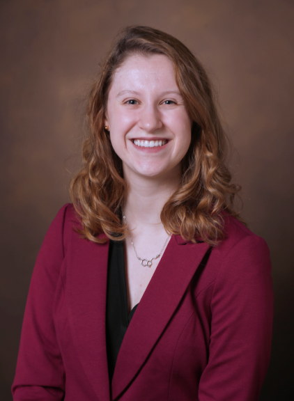Headshot of woman in pink blazer and gold background smiling 