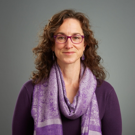 photo of Liza Sacheli, a light-skinned woman with long curly brown hair, wearing purple glasses