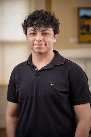 A photograph of Mina Rizk, wearing a black polo shirt and smiling at the camera.