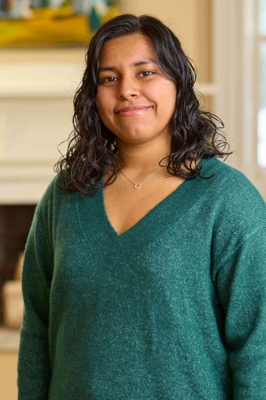 A photograph of Noemi Ponce, wearing a green sweater and smiling at the camera.