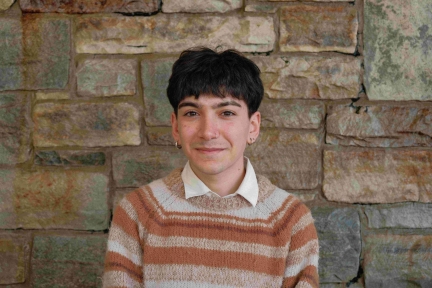 A photograph of Isak, wearing a striped sweater and smiling at the camera