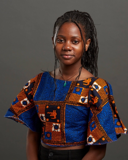 A photograph of Nawale, wearing an African-print top and looking at the camera.