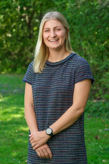 A photograph of Sarah Bauman-Kaye, wearing a blue dress and smiling at the camera. 