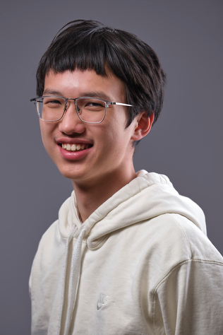 A photograph of Joseph Zou, wearing a white hoodie and smiling at the camera