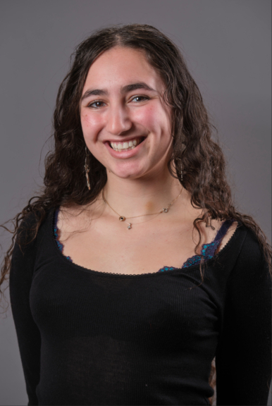 A photograph of Maya Atmani, wearing a black shirt and smiling at the camera