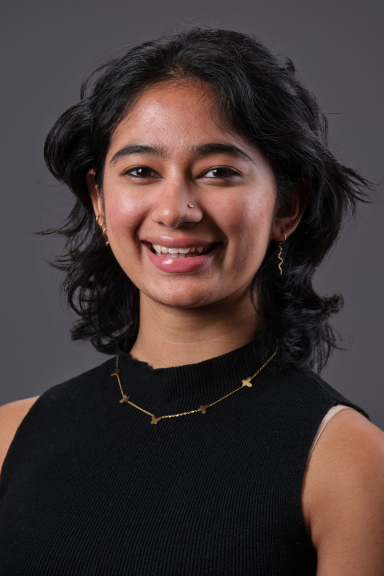 A photograph of Zaina Mahbub, wearing a black tank top and smiling at the camera