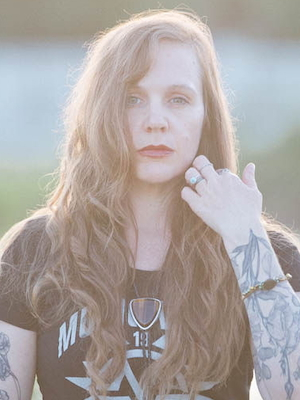 woman with long wavy brown hair wearing a black shirt and western jewelry