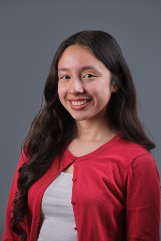 A photograph of Brianna Acosta-Garcia, wearing a red cardigan over a white shirt and smiling at the camera.