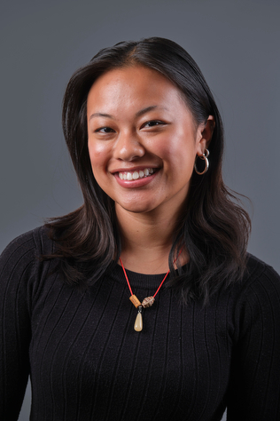 A photograph of Stella Marcellina, wearing a black long-sleeved T-shirt and smiling at the camera.