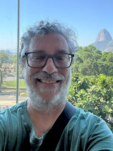 Headshot of Fernando Rocha smiling with foliage and mountains behind