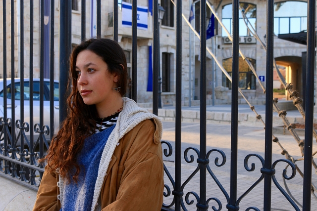 a young woman with long dark hair leans against an iron fence