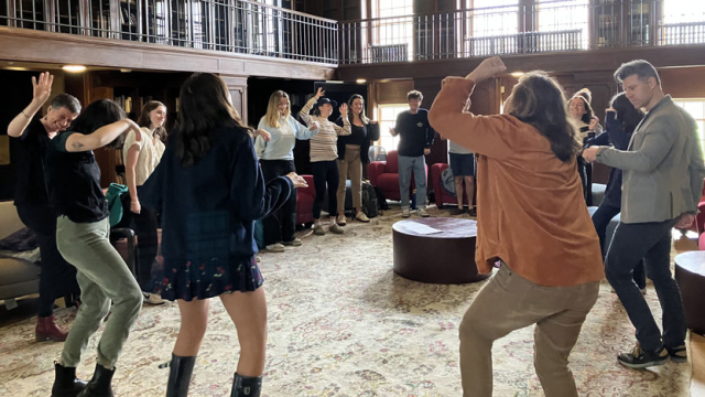 Students in a classroom workshop standing in a circle and moving their bodies.
