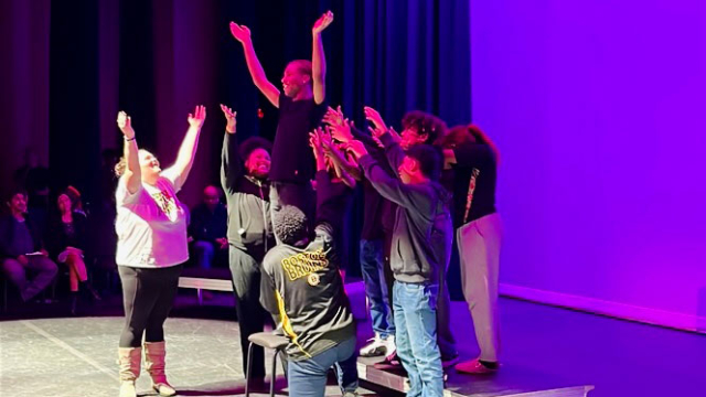 A cast performs a theatre piece in a purple light.
