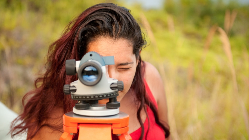 A student looks through a viewfinder, directly at the camera. 