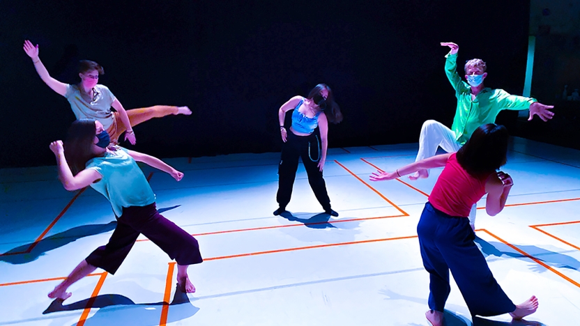 Five dancers dressed colorfully and masked in a wide circle