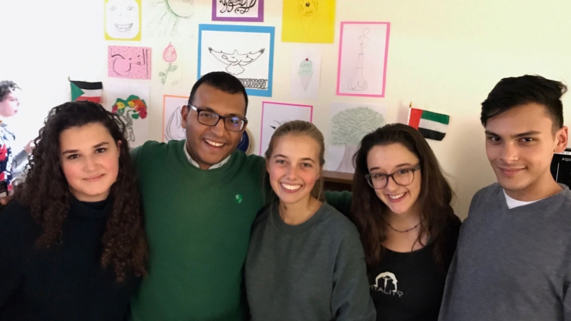 Arabic students gathering in front of artwork created in class.