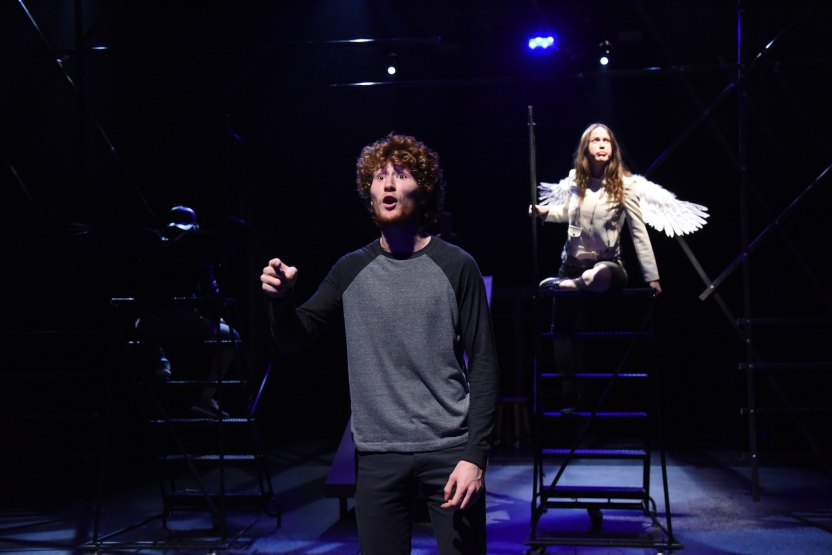 Actor looking out and pointing with actress behind him with wings