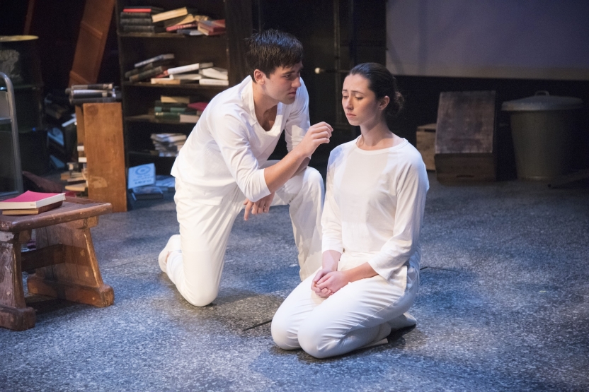 An actress kneeling with her eyes closed, and actor beside her with his hand near her face, both wearing all white