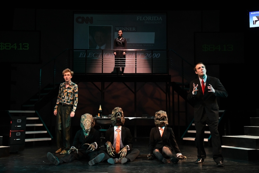 Two actors facing out, three actors between them sitting wearing dinosaur heads, one actress on balcony in background