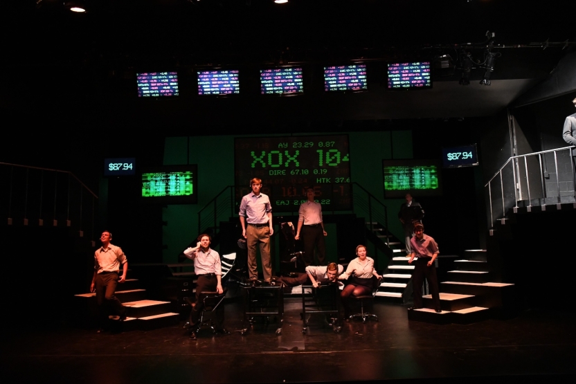 Seven actors as office workers in front of a digital projection of green numbers