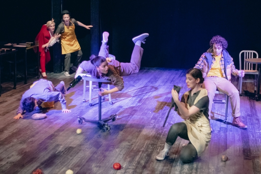 Produce scattered across the ground as actors are wild amongst the ground, chairs, and tables