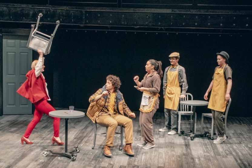 Actor angrily raising a chair above their head at other actors