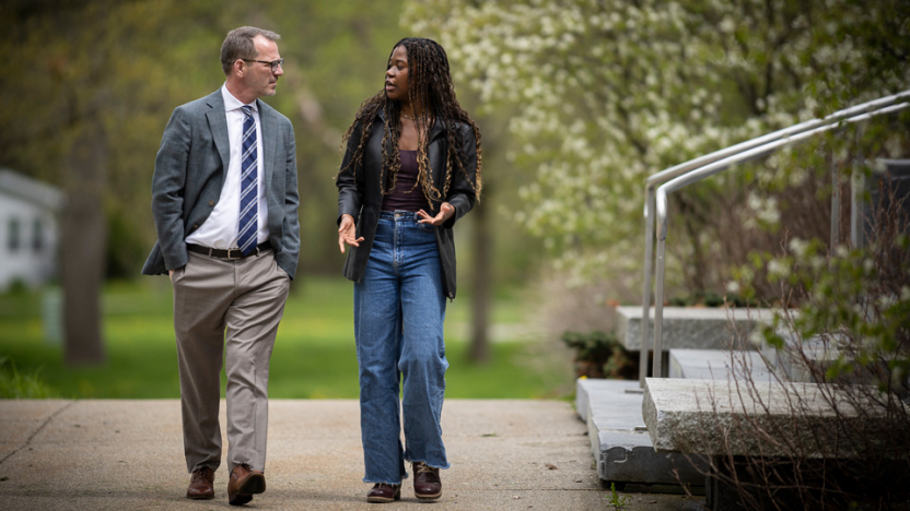 President Ian Baucom and a student walk past the Axinn Center while talking.