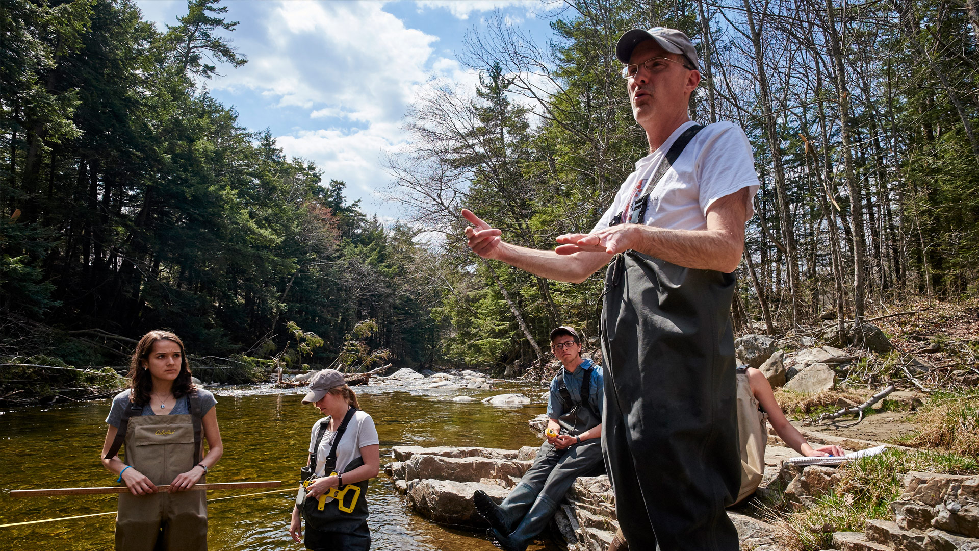 A science professor leads student in a field exercise in the Otter Creek near campus.