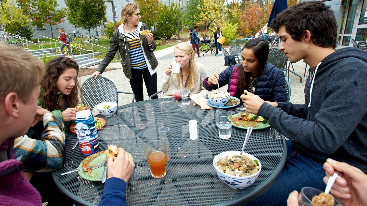 Several Middlebury students sit at an outdoor patio table talking and eating a meal.