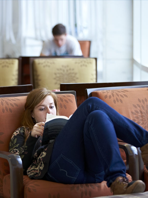 A student reads curled up in a comfortable chair at Middlebury's Davis Family Library.