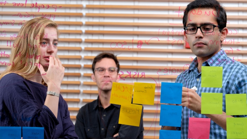 Three Middlebury students contemplating messages on post it notes.
