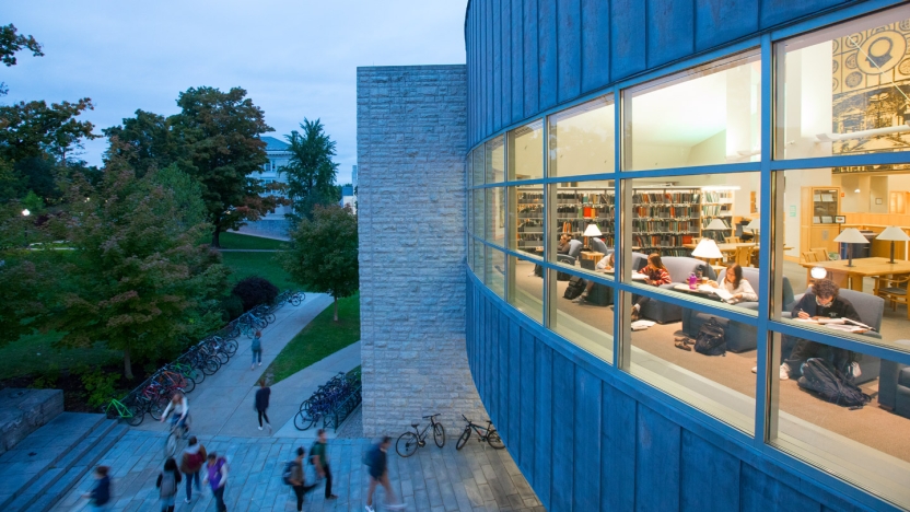 Exterior view of Middlebury's Davis Family Library at dusk, with a view through the lighted windows to students inside studying.