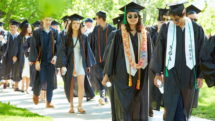 A procession of Middlebury grads walks toward the ceremony.
