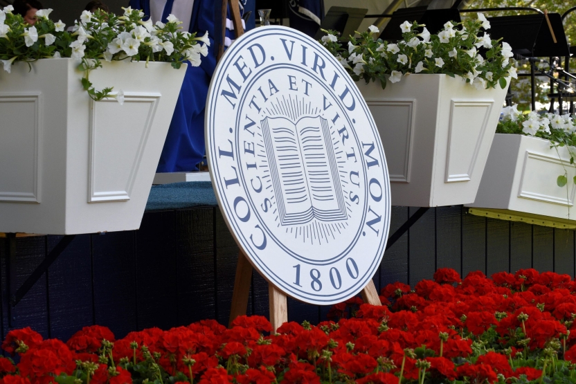 College seal in front of commencement stage, surrounded by flowers
