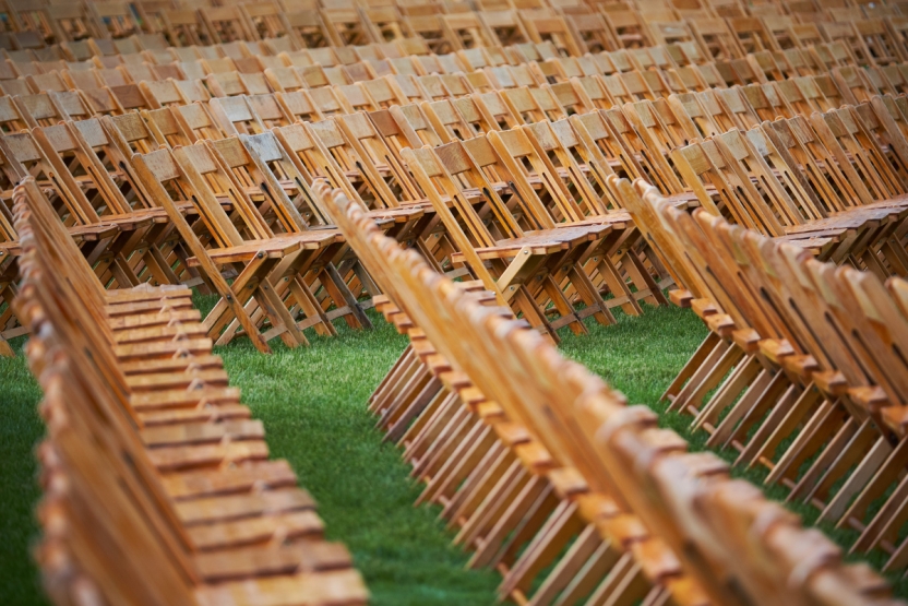 Rows of wooden folding chairs on a grass lawn