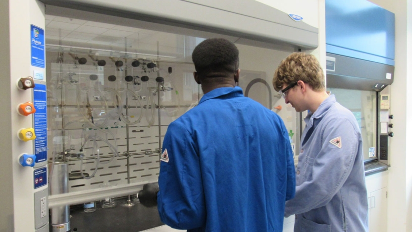 Researchers analyzing TLC plates in a fume hood (left to right, Abdul Abubakari and William Holzman)
