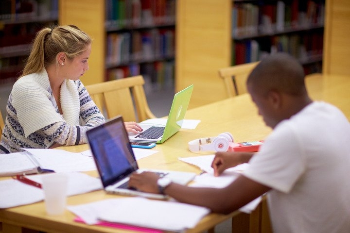two students complete assignments on laptops