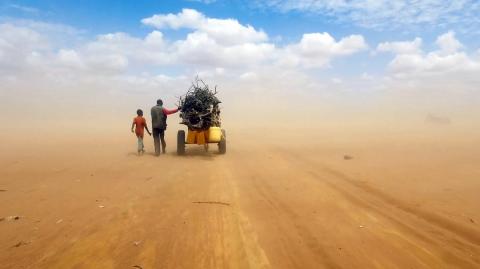 Man and boy on a dusty dirt road following a wagon filled with debris